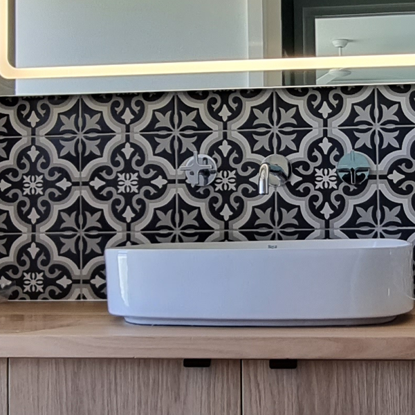 White basin on wooden vanity with LED-lit mirror and black and white graphic tiles