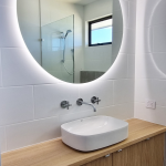 Wooden vanity with rounded rectangular basin and large LED-lit circular mirror