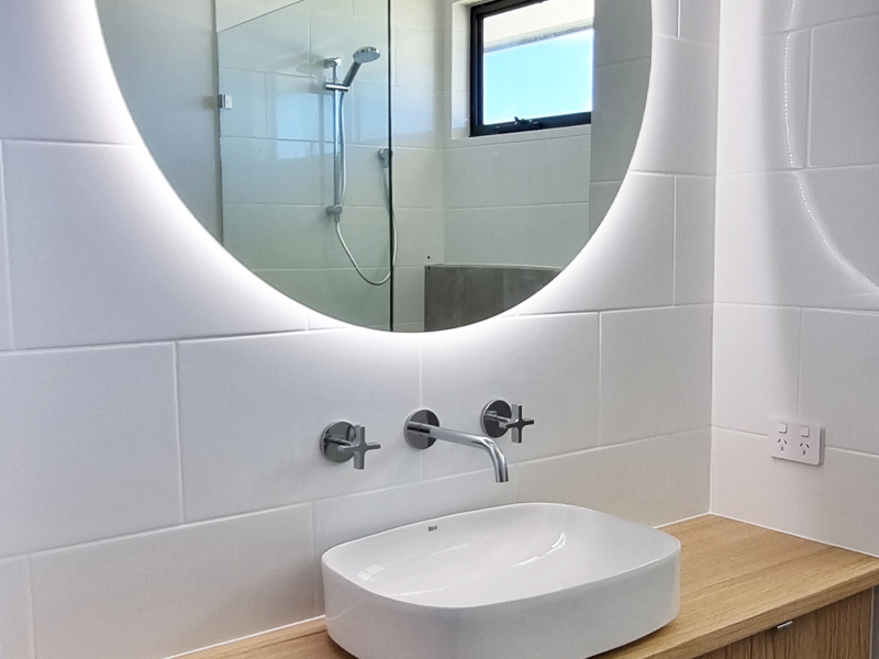 Wooden vanity with rounded rectangular basin and large LED-lit circular mirror